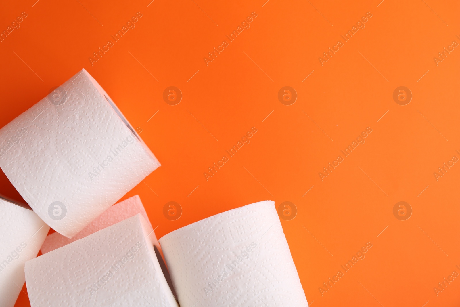 Photo of Soft toilet paper rolls on orange background, flat lay. Space for text