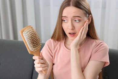 Photo of Emotional woman holding brush with lost hair at home. Alopecia problem