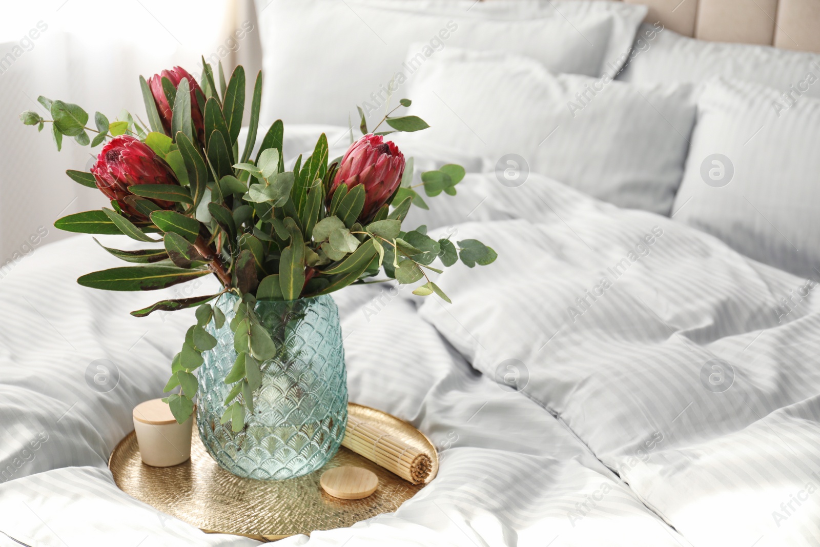 Photo of Vase with bouquet of beautiful Protea flowers on bed indoors