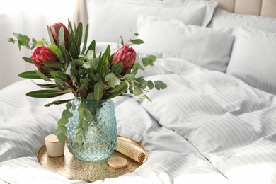 Vase with bouquet of beautiful Protea flowers on bed indoors