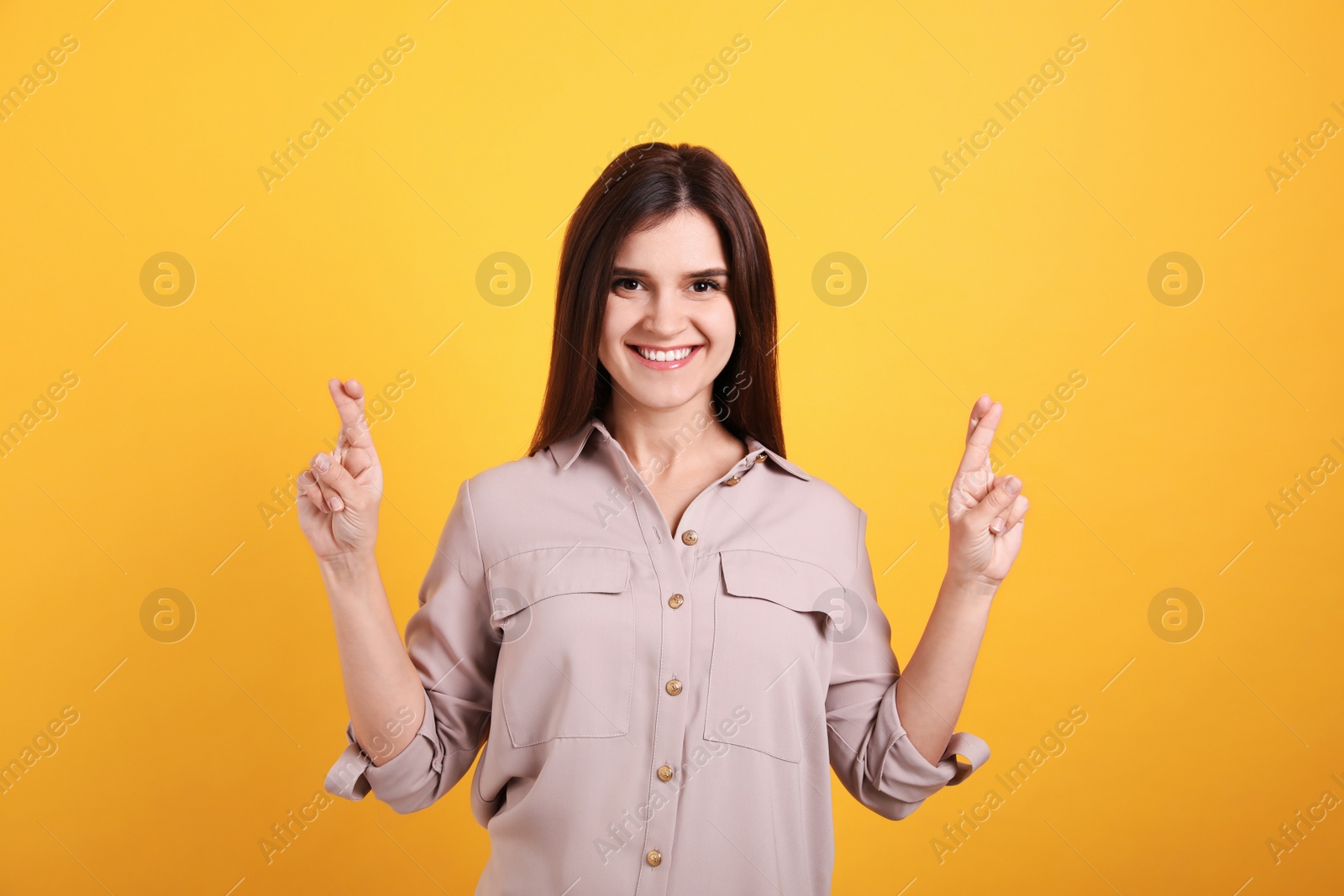 Photo of Happy young woman crossing fingers on yellow background. Dealing with stress