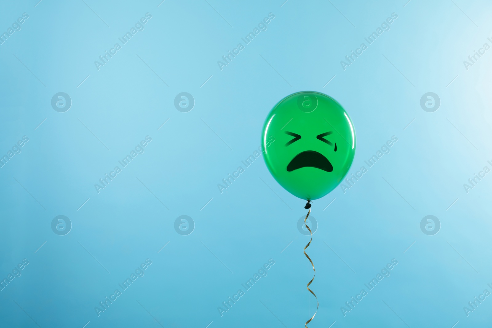 Image of Green balloon with sad face on light blue background. Space for text