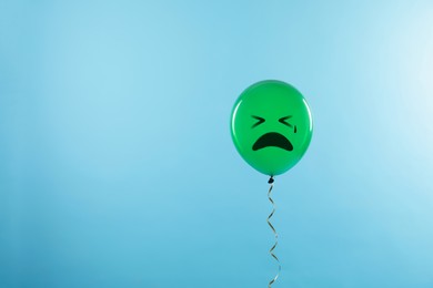 Green balloon with sad face on light blue background. Space for text