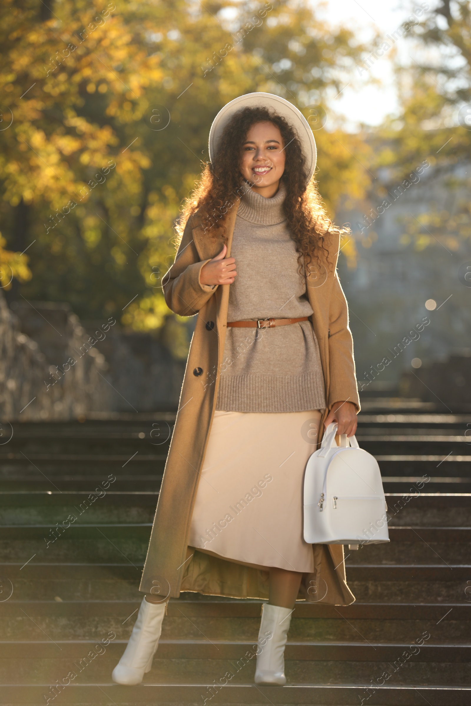 Photo of Full length portrait of beautiful African-American woman with stylish white backpack on stairs outdoors