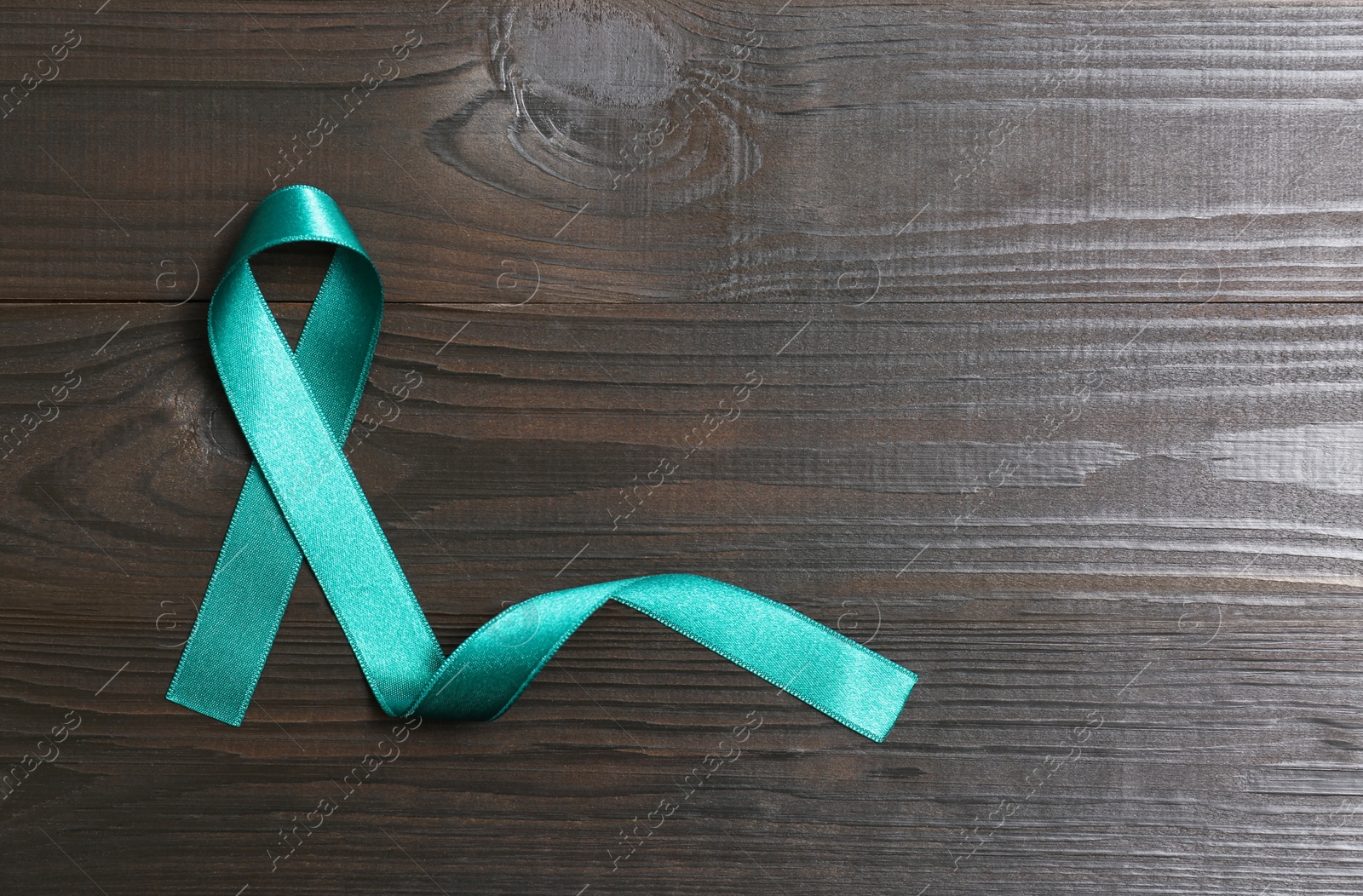 Photo of Teal awareness ribbon on wooden background, top view with space for text. Symbol of social and medical issues