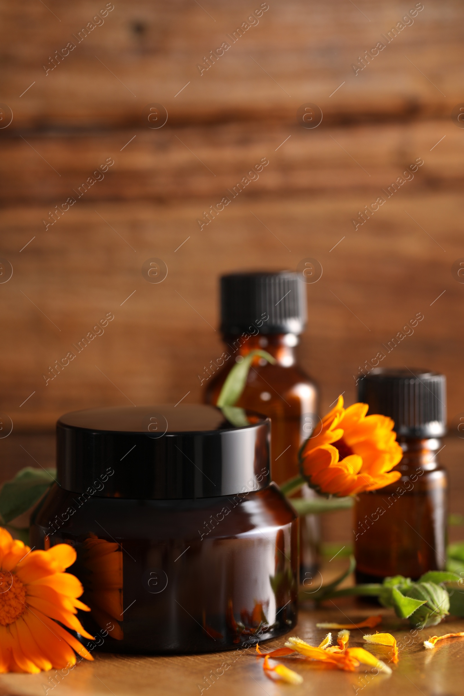 Photo of Different cosmetic products and beautiful calendula flowers on wooden table, closeup