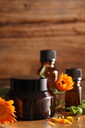 Different cosmetic products and beautiful calendula flowers on wooden table, closeup