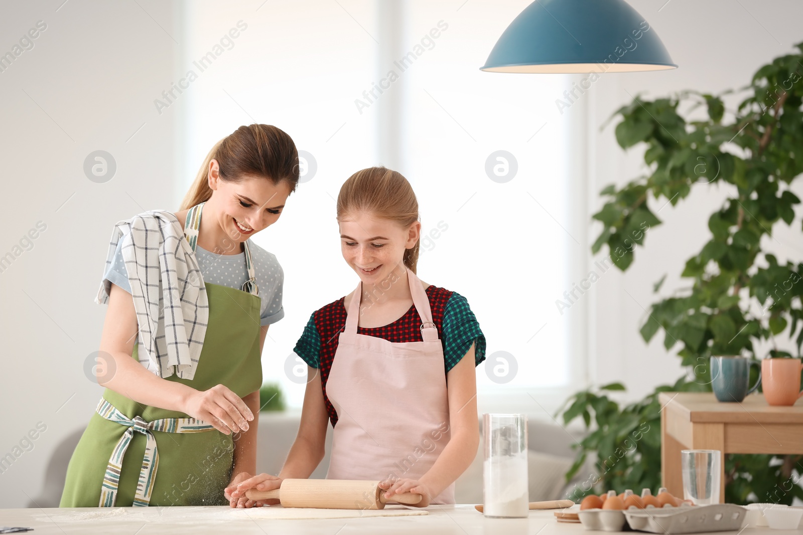 Photo of Mother and her daughter making dough at table in kitchen