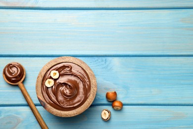 Spoon and bowl of tasty chocolate hazelnut spread on light blue wooden table, flat lay. Space for text
