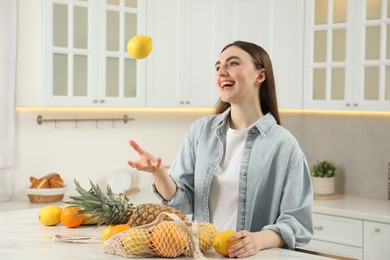 String bag with fresh fruits on light marble table. Woman throwing lemon in kitchen