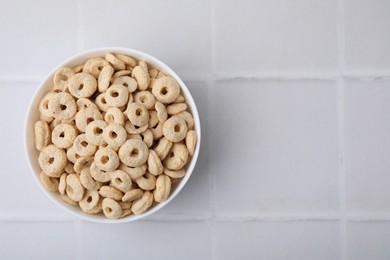 Photo of Tasty cereal rings in bowl on white tiled table, top view. Space for text