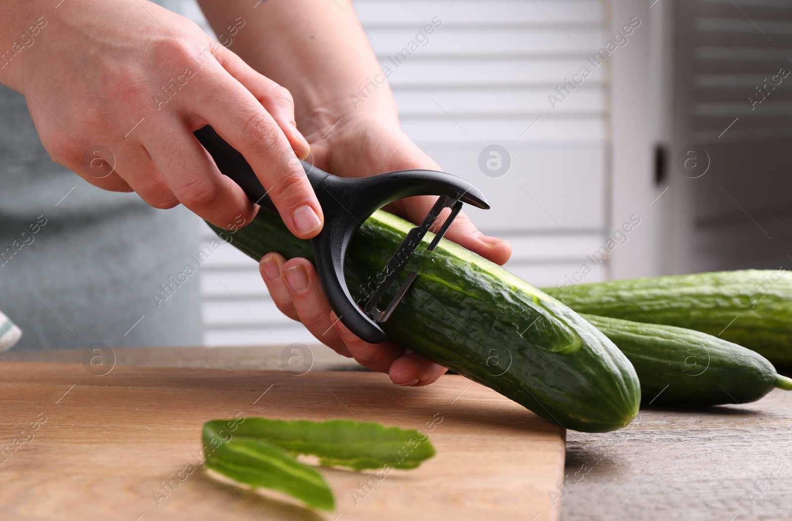 Photo of Woman peeling cucumber at wooden table indoors, closeup