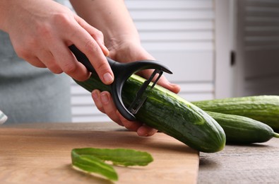 Photo of Woman peeling cucumber at wooden table indoors, closeup