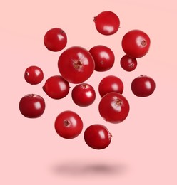 Image of Delicious ripe cranberries falling on light pink background