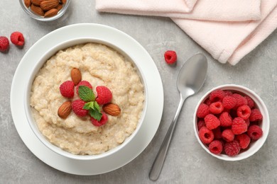 Photo of Tasty oatmeal porridge with raspberries and almond nuts served on light grey table, flat lay