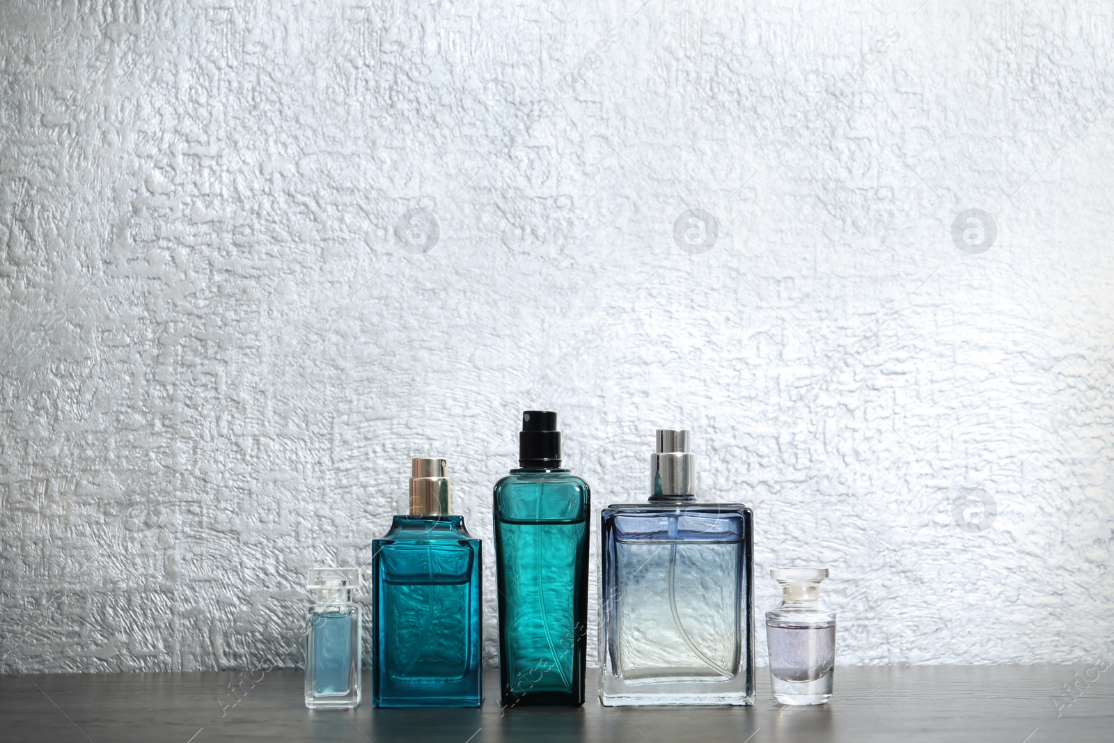 Photo of Different perfume bottles on table against color background