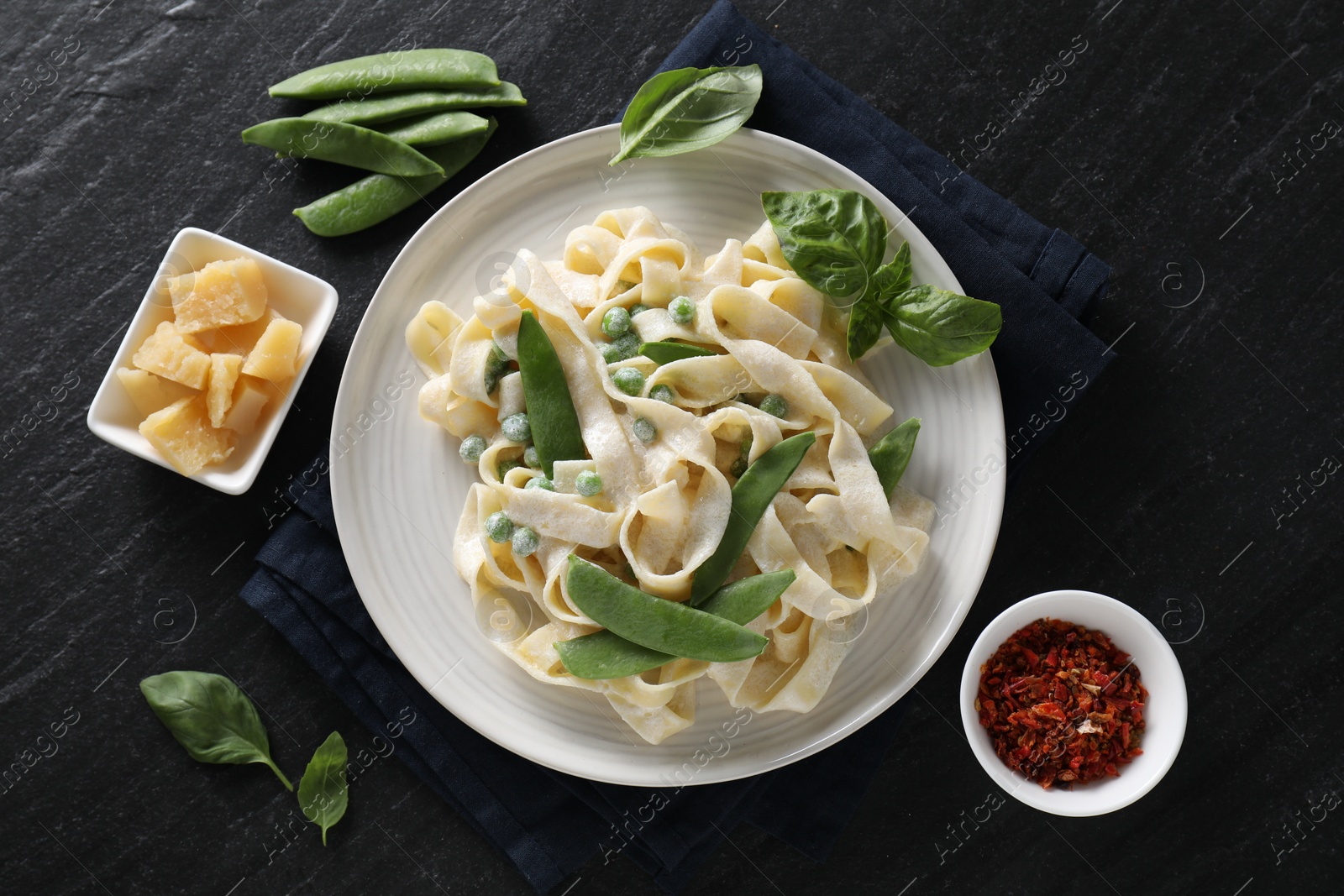 Photo of Delicious pasta with green peas and ingredients on black table, flat lay