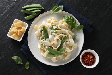 Delicious pasta with green peas and ingredients on black table, flat lay