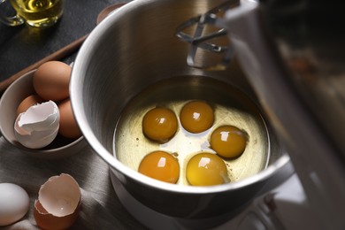 Photo of Making dough. Raw eggs in bowl of stand mixer and ingredients on black table, closeup