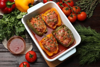 Photo of Tasty stuffed peppers in dish and ingredients on wooden table, flat lay