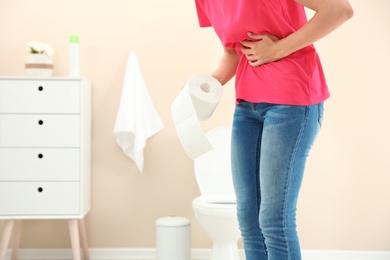 Young woman with bath tissue standing near toilet bowl at home