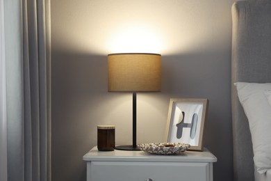 Stylish lamp and decor on white nightstand in bedroom