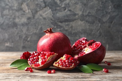 Photo of Ripe pomegranates and leaves on table against grey background. Space for text