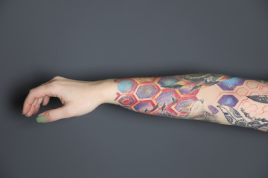 Woman with colorful tattoos on arm against dark grey background, closeup