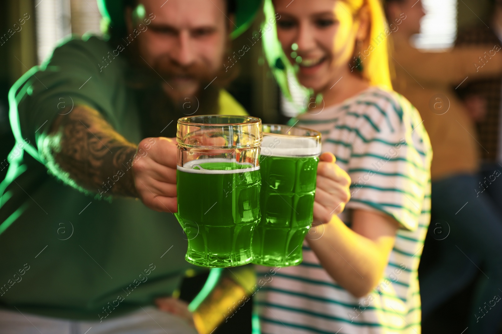 Photo of Young woman and man toasting with green beer in pub, focus on glasses. St. Patrick's Day celebration