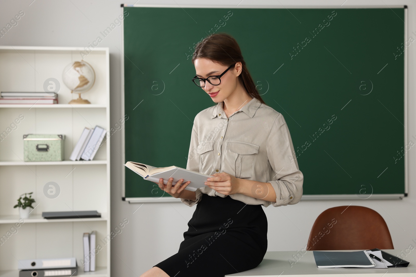 Photo of Beautiful young teacher reading book in classroom