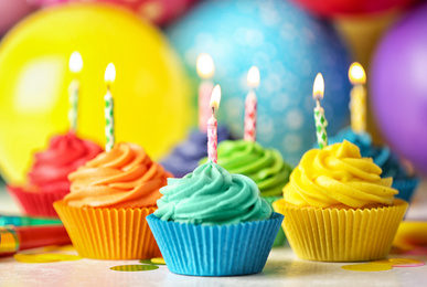 Photo of Delicious birthday cupcakes with cream and burning candles on table