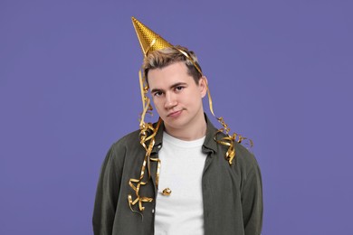 Photo of Sad young man with party hat on purple background