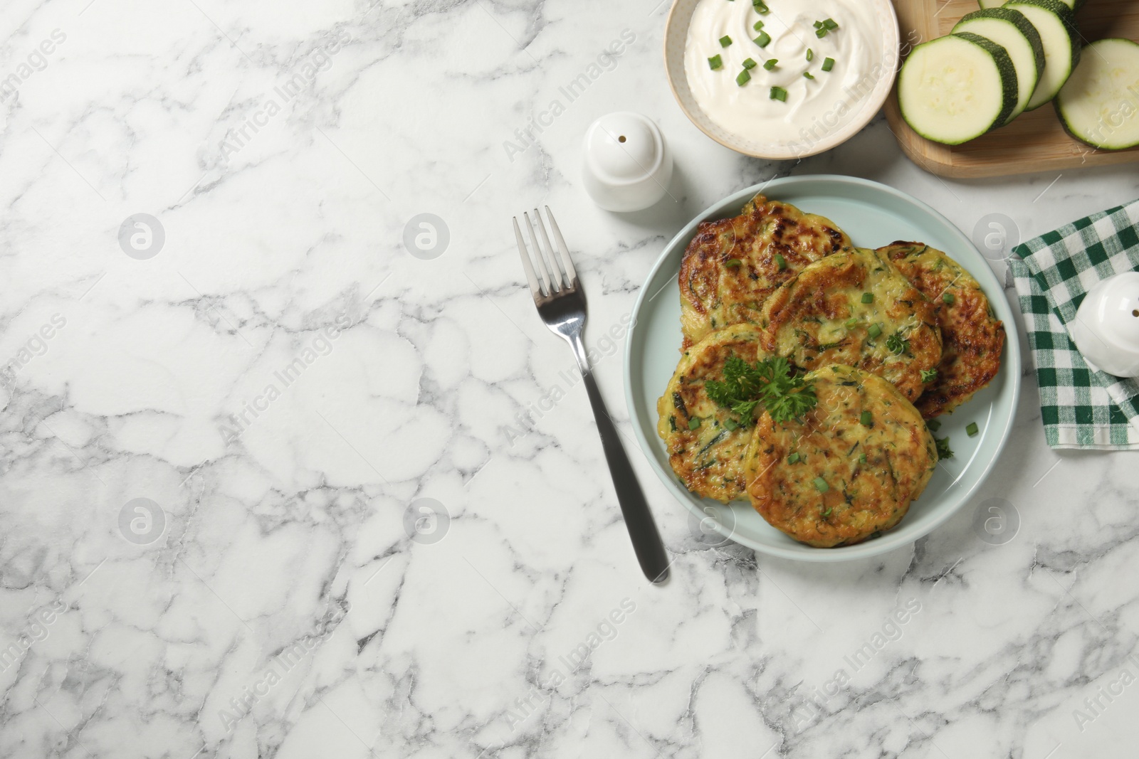 Photo of Delicious zucchini fritters served on white marble table, flat lay. Space for text