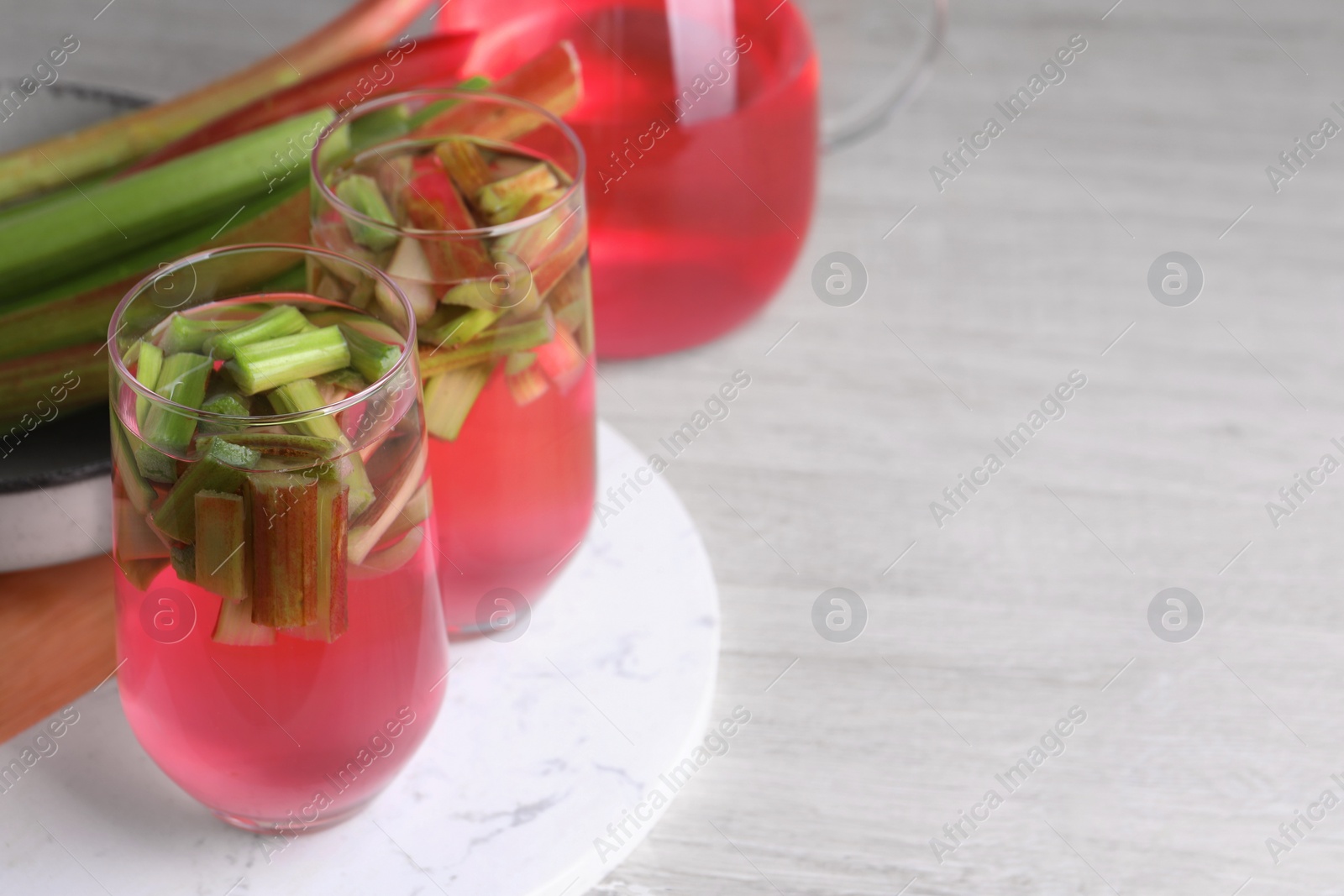 Photo of Glasses of tasty rhubarb cocktail on white wooden table, space for text