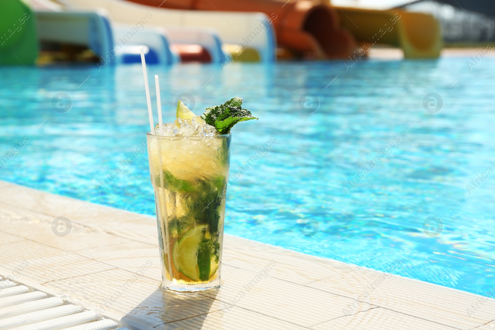 Photo of Glass of delicious mojito near swimming pool, space for text. Refreshing drink