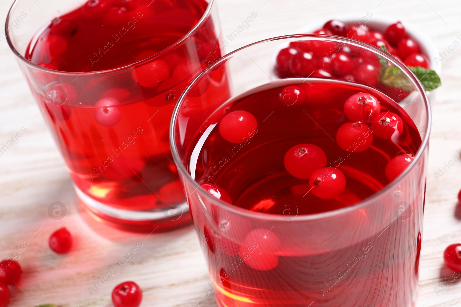Photo of Tasty cranberry juice in glasses and fresh berries on white wooden table, closeup