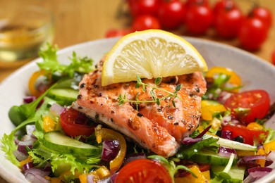 Photo of Bowl with tasty salmon, lemon and mixed vegetables on table, closeup