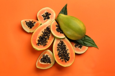 Photo of Fresh ripe papaya fruits with green leaves on orange background, flat lay