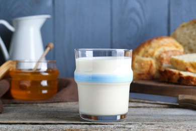 Glass with milk, honey and bread on rustic wooden table