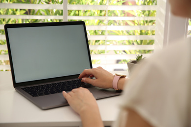 Photo of Woman working with modern laptop at white table, closeup. Space for design