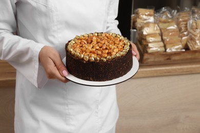 Photo of Baker holding delicious cake in cafe, closeup. Space for text