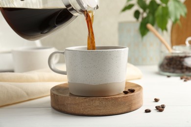 Photo of Pouring coffee into cup at white wooden table, closeup