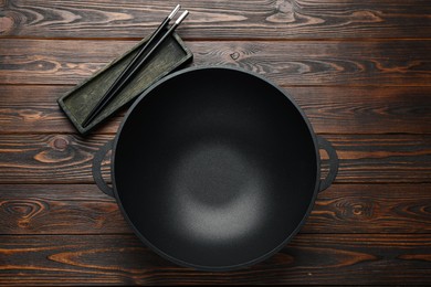 Empty iron wok and chopsticks on wooden table, flat lay