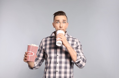 Emotional man with popcorn and beverage during cinema show on grey background