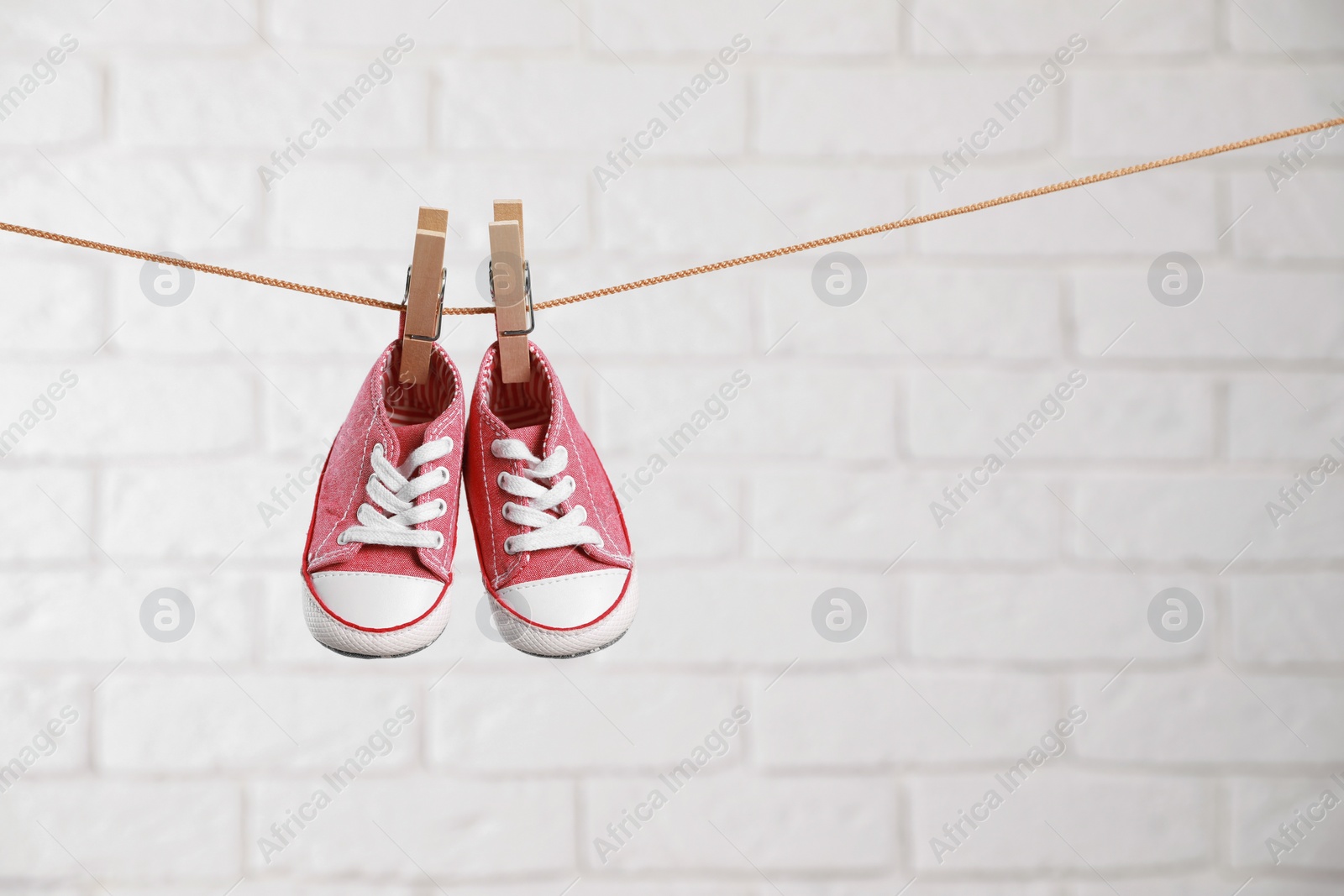 Photo of Cute pink baby sneakers drying on washing line against white brick wall. Space for text