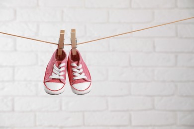 Cute pink baby sneakers drying on washing line against white brick wall. Space for text