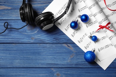 Flat lay composition with Christmas decorations, headphones and music sheets on blue wooden table, space for text