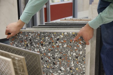 Photo of Man choosing tile among different samples in store, closeup