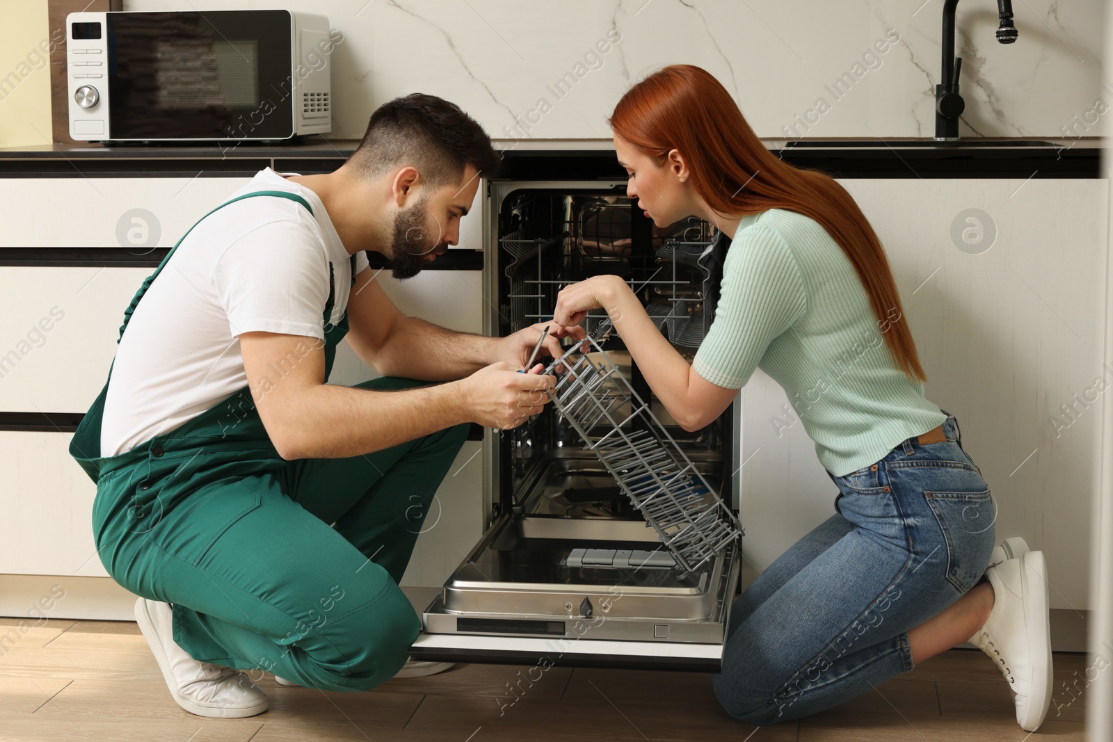 Photo of Woman looking how serviceman repairing her dishwasher in kitchen