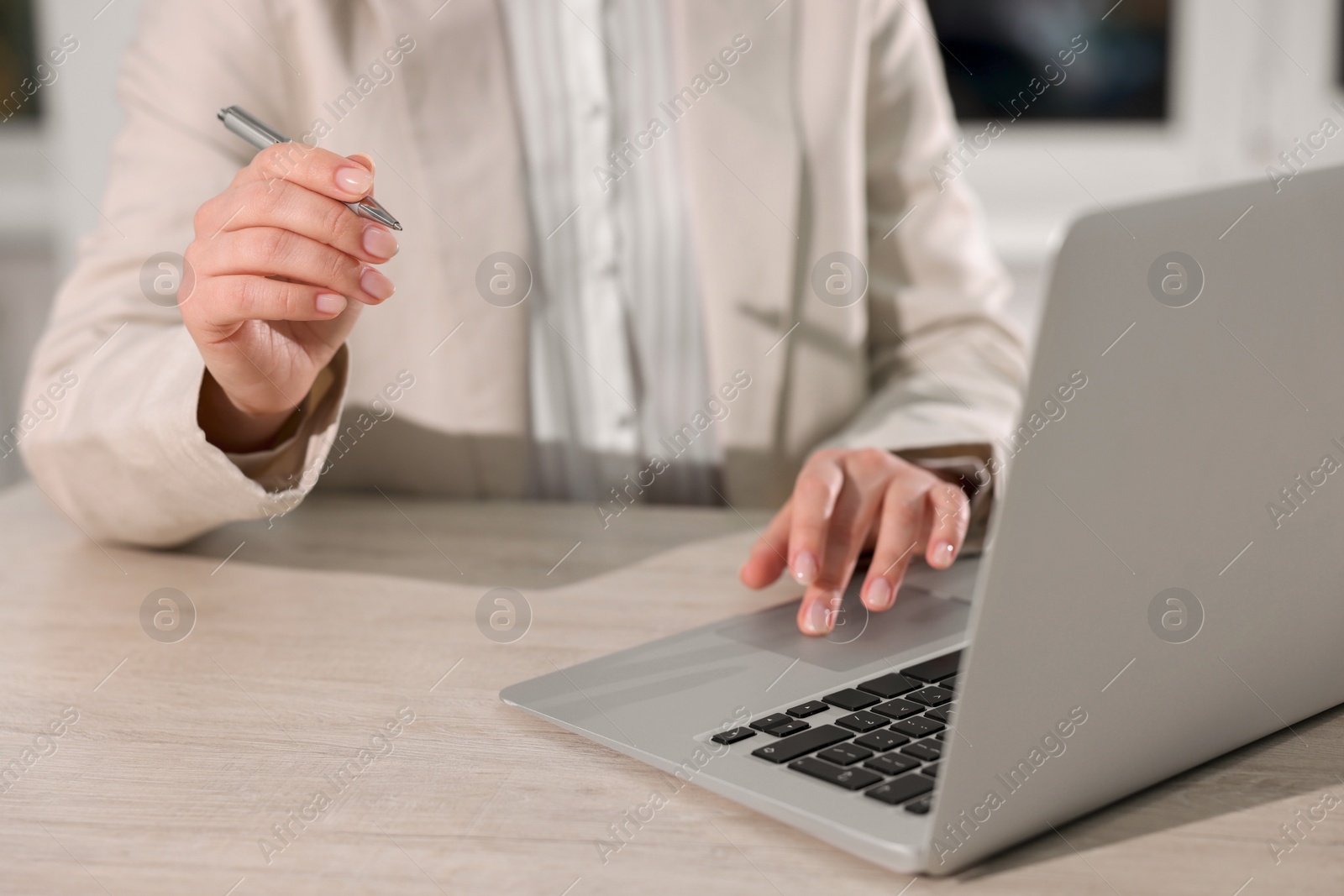 Photo of Woman with pen working on laptop at wooden table, closeup. Electronic document management